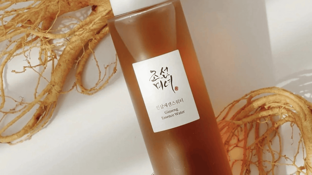 En flaska av Beauty of Joseon Ginseng Essence Water omgiven av torkade ginsengrötter på en ljus bakgrund, vilket framhäver dess naturliga ingredienser.