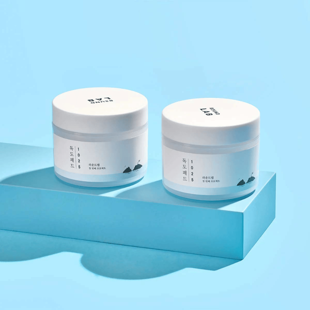 Deux pots blancs de 1025 Dokdo Pads, placés sur une étagère bleu clair qui projette un reflet, sur un fond bleu.