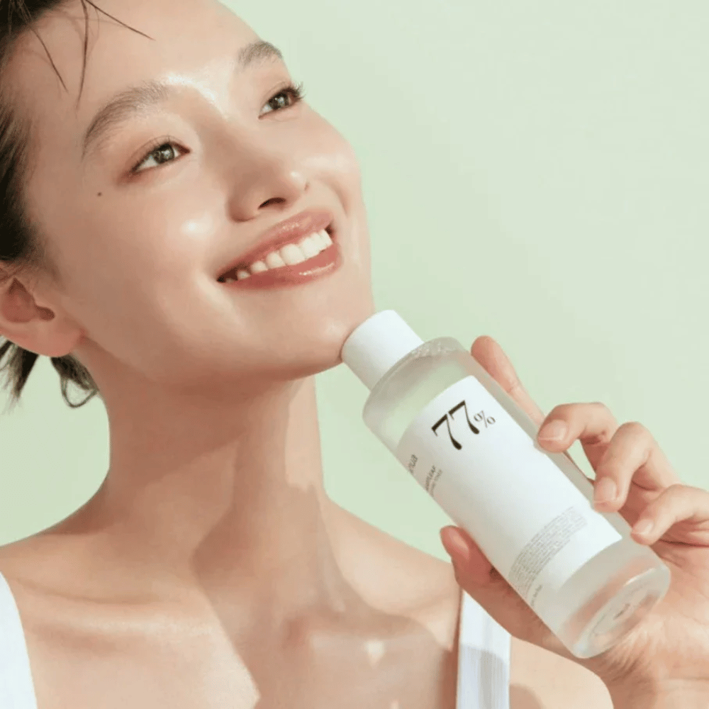Une femme apaise sa peau sensible avec une bouteille Heartleaf 77% Soothing Toner de Anua, contenant un extrait de feuille de caméléon.