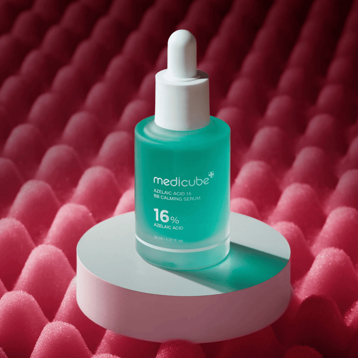 Image produit de Medicube Azelaic Acid 16 BB Calming Serum placée sur un podium blanc avec un fond rose texturé qui met en valeur le profil apaisant et améliorant la peau du sérum.