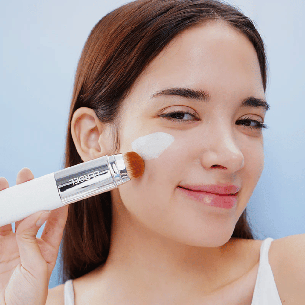 Un modèle applique ELROEL Blanc Cover Cream Stick concealer sur la joue avec un pinceau intégré pour une couverture naturelle et uniforme.