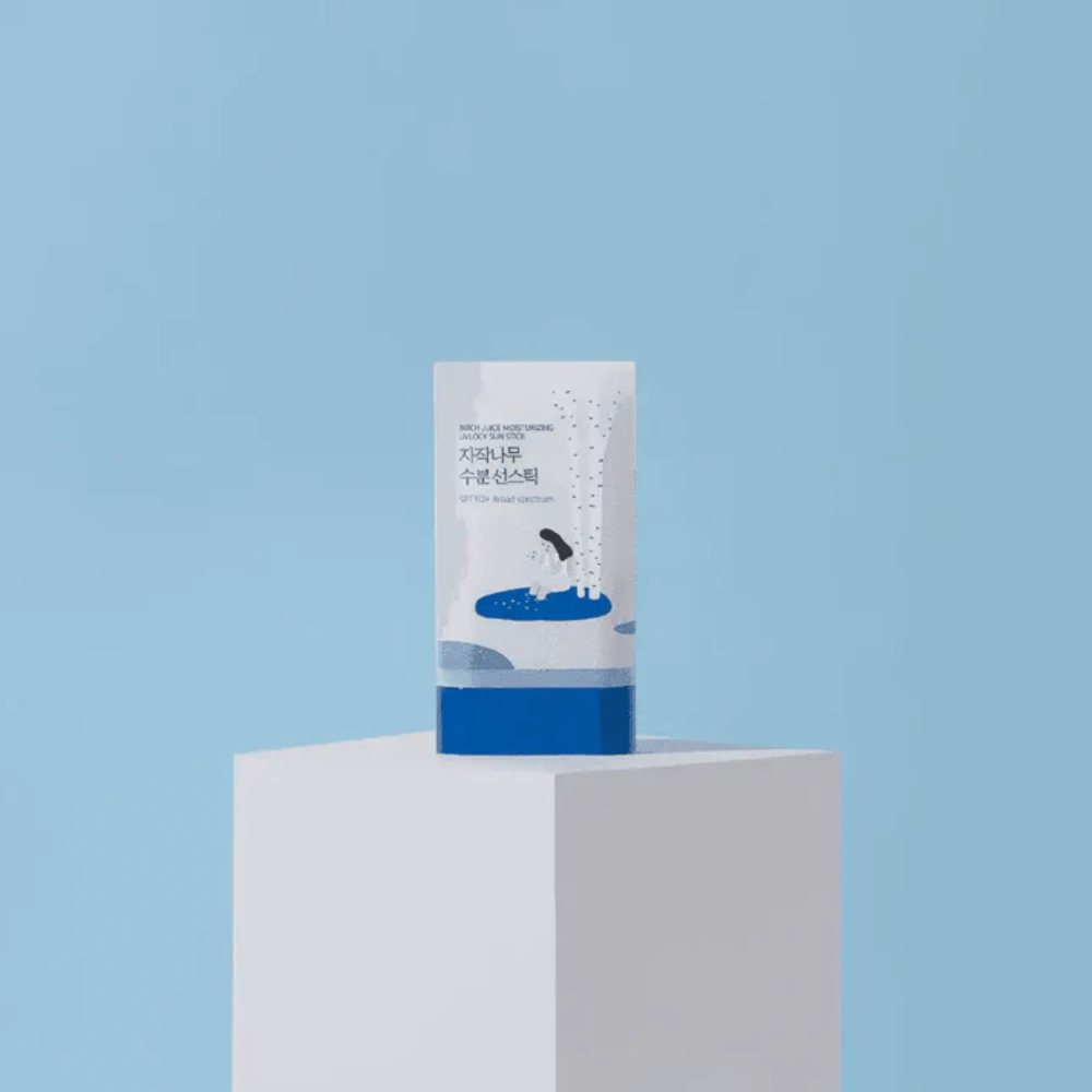 ROUND LAB Birch Juice Moisturizing Sun Stick SPF50+ est posé sur un piédestal sur fond bleu – une protection solaire hydratante en format stick