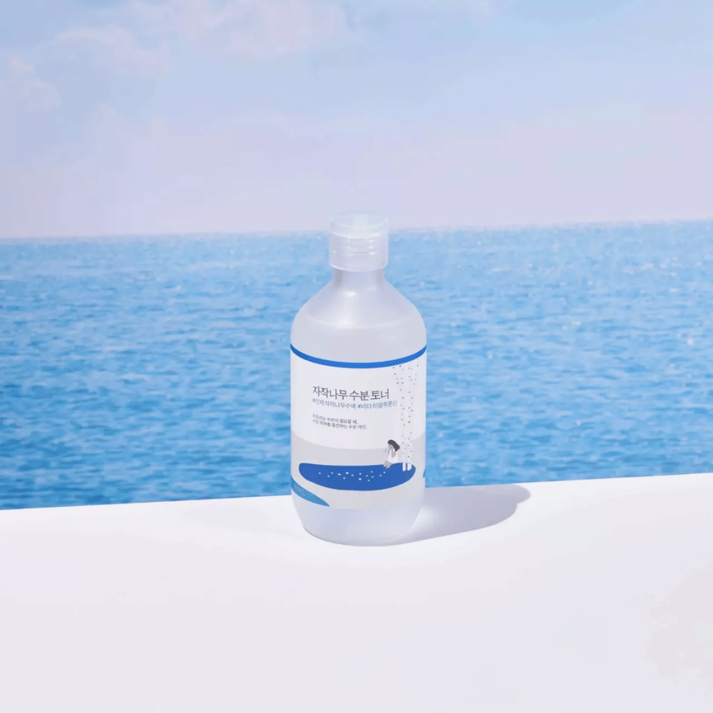 Flacon de ROUND LAB Birch Juice Moisturizing Toner posé sur une surface blanche avec la mer et un ciel bleu en arrière-plan
