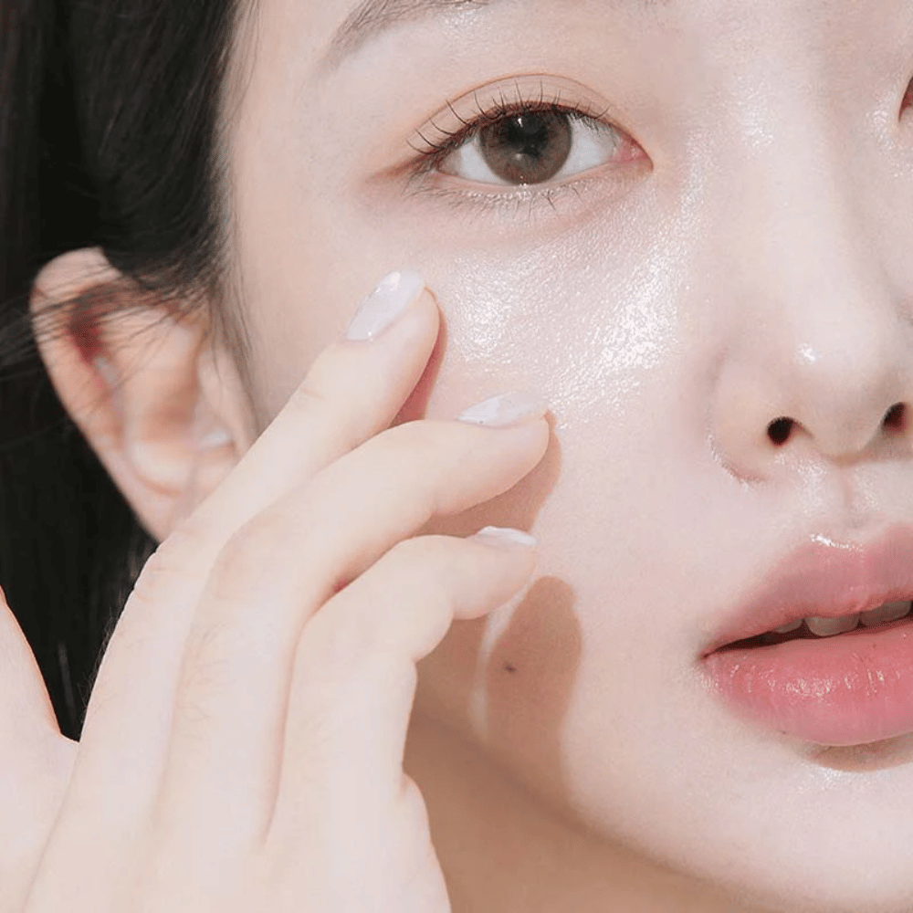 Gros plan sur une femme appliquant de la crème pour les yeux sous l'œil avec le bout des doigts. La peau semble hydratée, brillante et soignée avec un éclat naturel.