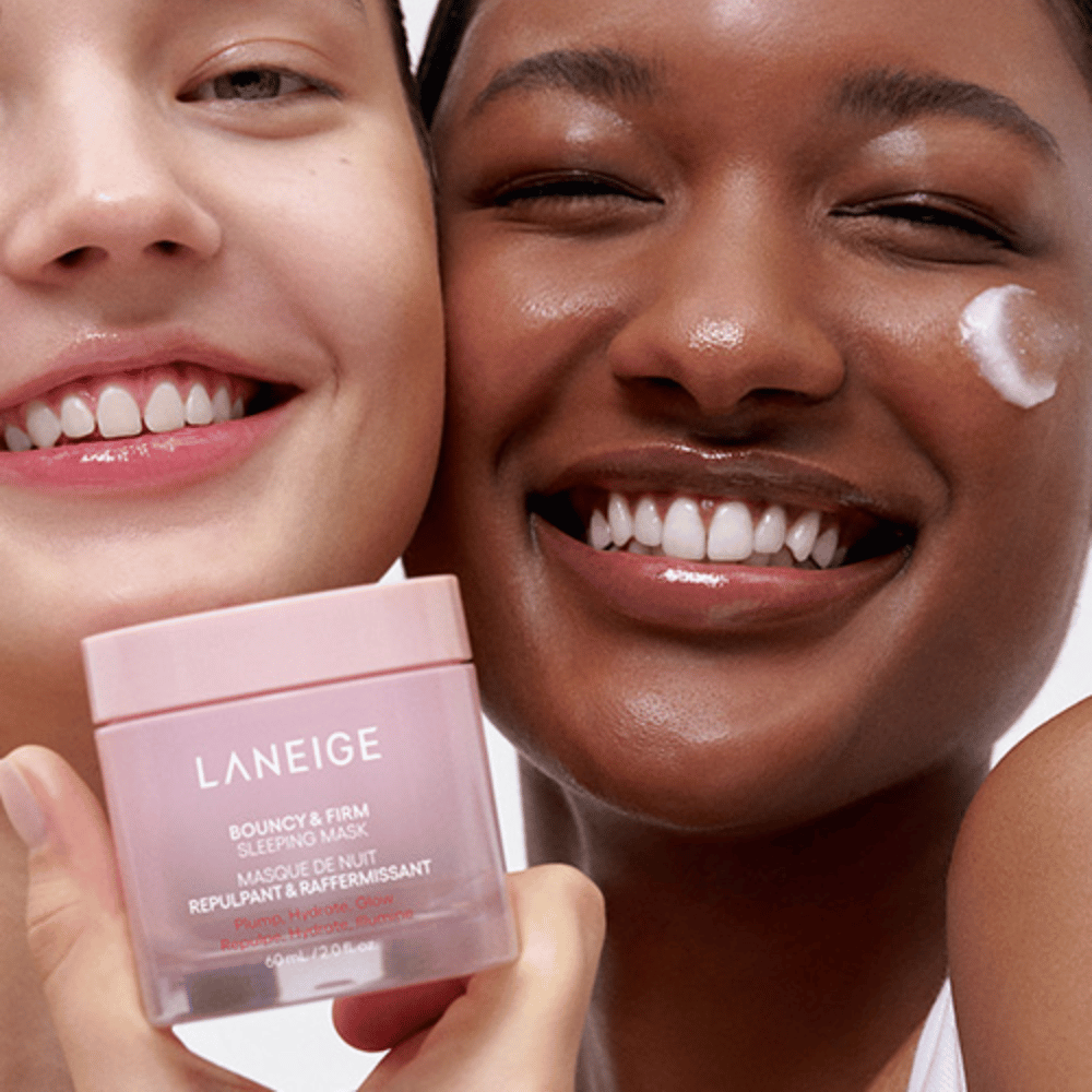 Deux personnes sourient et tiennent Laneige Bouncy & Firm Sleeping Mask. L'une a appliqué le masque sur sa joue, et le produit est clairement visible dans leurs mains. Le masque est dans un pot rose et est commercialisé comme "Plump, Hydrate, Glow."
