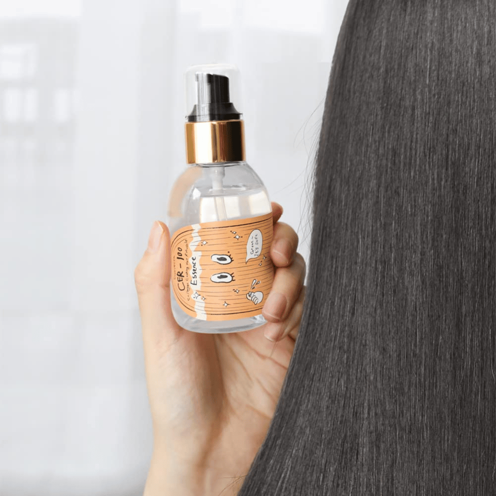 Une personne tient CER-100 Hair Essence à côté de longs cheveux brillants pour montrer la douceur et le soin.