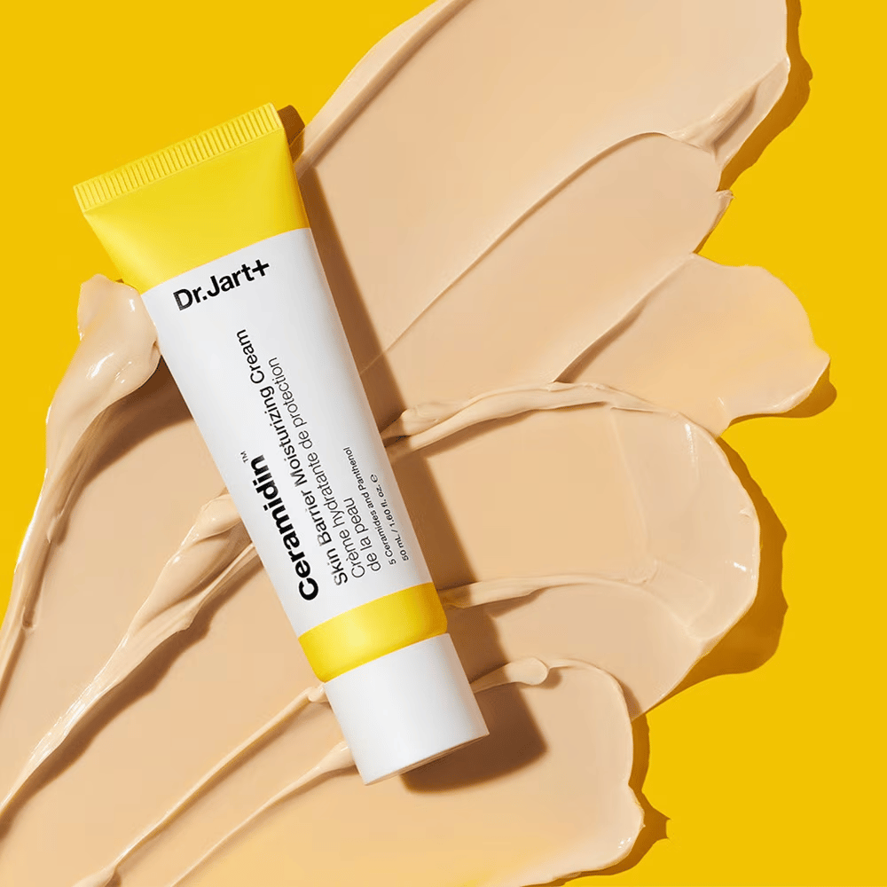 Tube avec Dr. Jart+ Ceramidin Skin Barrier Moisturizing Cream sur un fond jaune avec de la crème étalée.