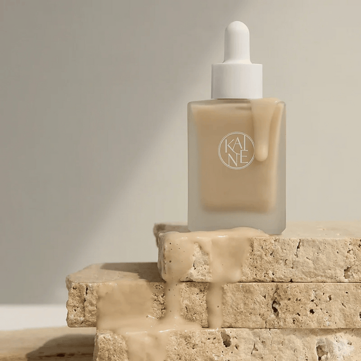 KANE Chaga Collagen Charging Serum i en frostad glasflaska med pipett. Krämig textur rinner ner över naturliga stenar i ett mjukt och minimalistiskt ljus.
