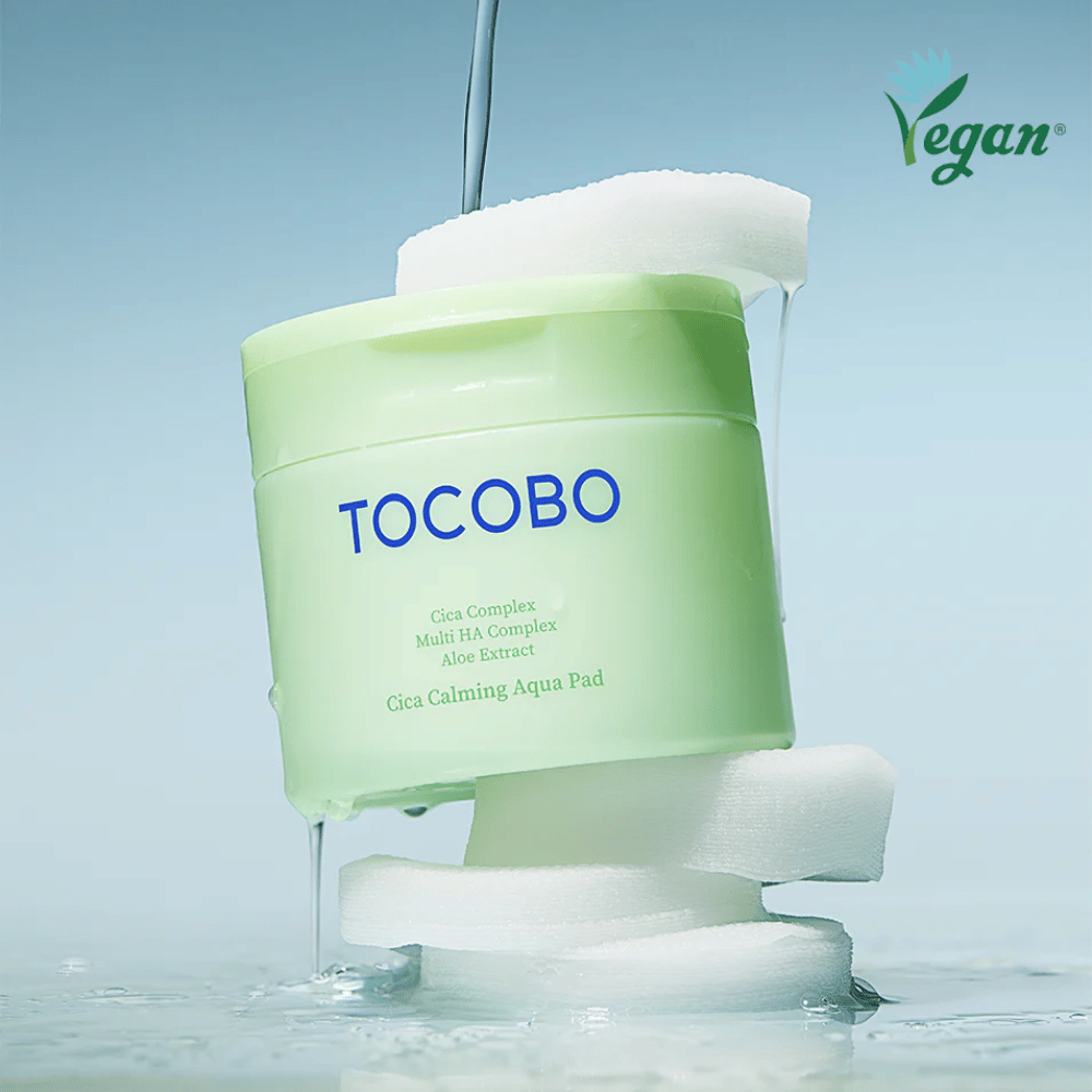 TOCOBO Cica Calming Aqua Pad placé entre des pads toner visage avec de l’essence qui s’écoule. Le symbole vegan souligne la formulation végane du produit et son profil respectueux de la peau.
