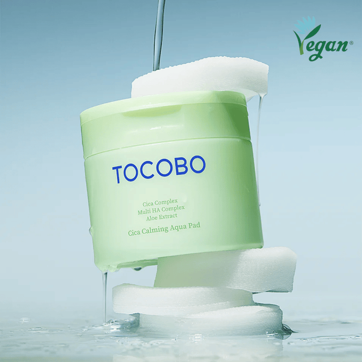 TOCOBO Cica Calming Aqua Pad placé entre des pads toner visage avec de l’essence qui s’écoule. Le symbole vegan souligne la formulation végane du produit et son profil respectueux de la peau.