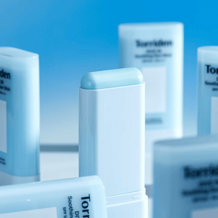 Gros plan sur Torriden DIVE IN Soothing Sun Stick montrant la formule douce de protection solaire au format stick, avec plusieurs produits en arrière-plan.
