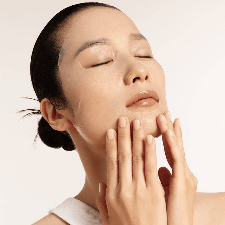 Modèle avec peau hydratée et éclatante appliquant Masque tissu, focus sur éclat, teint uniforme et glow.