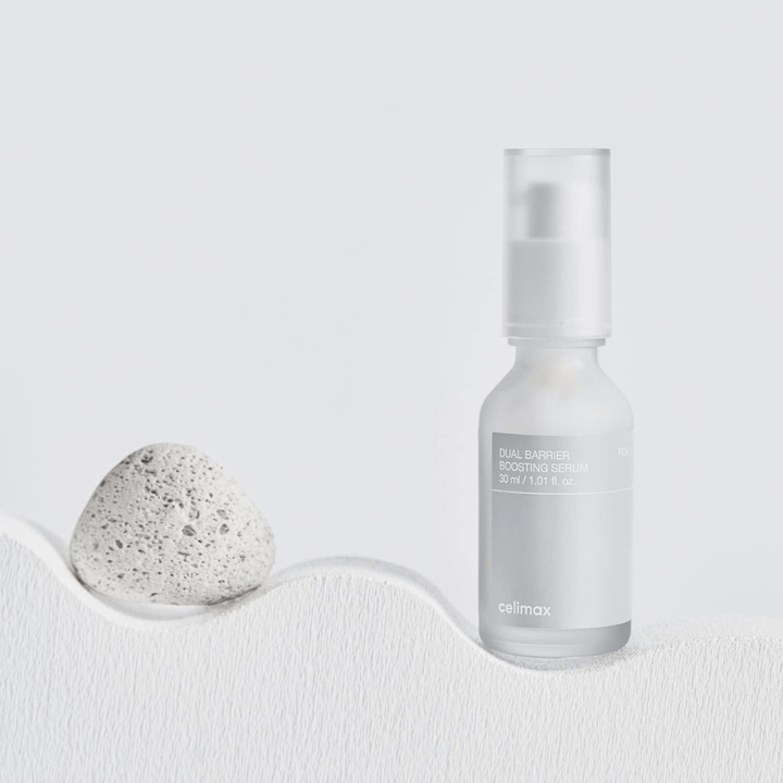 Celimax Dual Barrier Boosting Serum placé sur textile avec pierre, image de produit apaisante qui signale hydratation et barrière cutanée renforcée.