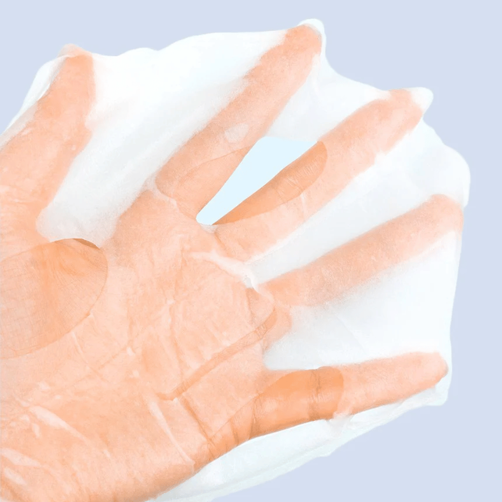 Un masque facial transparent et humide est tenu sur une main contre un fond bleu clair. Le masque est conçu pour couvrir le visage avec des espaces pour les yeux et la bouche.