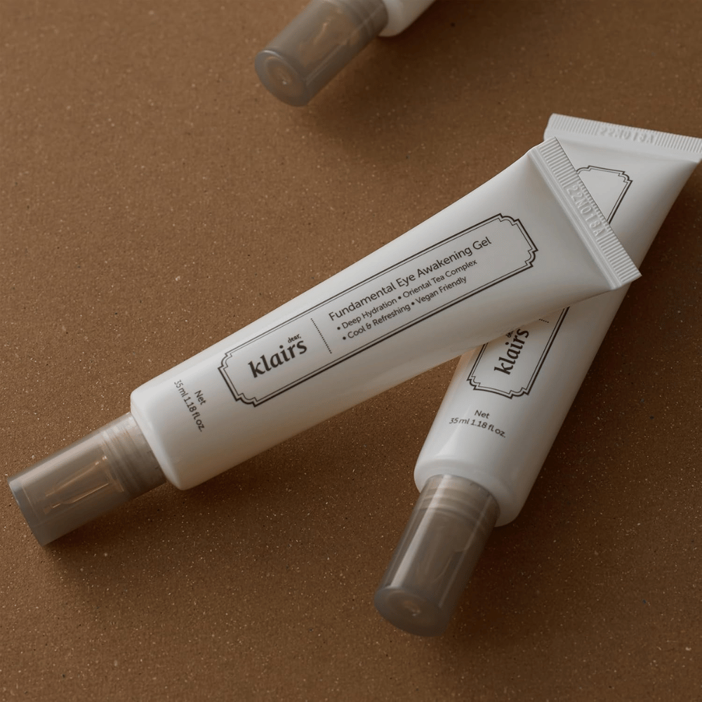Image lifestyle avec deux tubes de Klairs Fundamental Eye Awakening Gel placés sur un fond brun chaud. La composition met en valeur le design élégant du produit et son aspect premium, tout en mettant l’accent sur le soin du contour des yeux et l’hydratation.