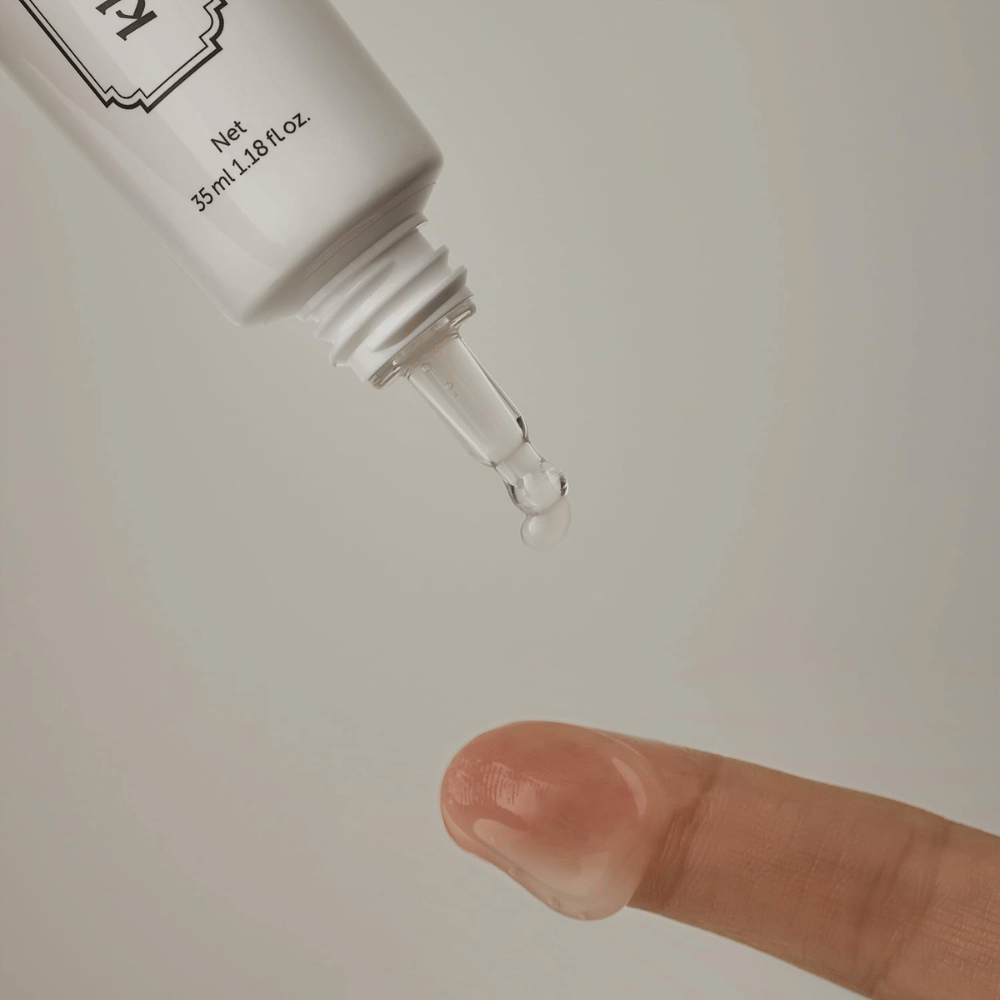 Image en gros plan où un gel clair et léger est appliqué depuis l’embout fin sur un doigt. L’image illustre la texture transparente à base de gel du produit ainsi que l’application précise autour du contour des yeux.