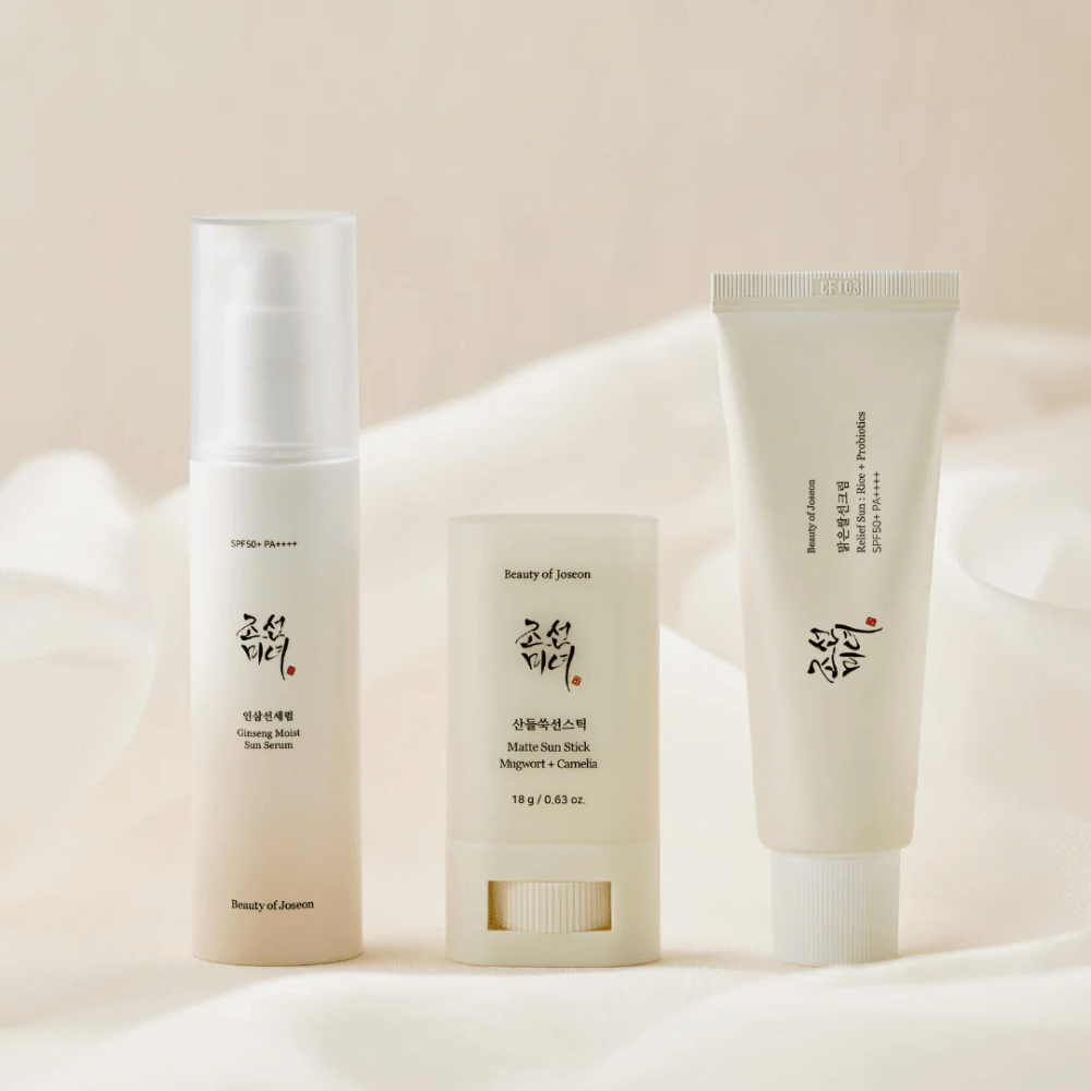 Trois produits solaires de Beauty of Joseon – Ginseng Moist Sun Serum, Matte Sun Stick et Relief Sun Rice + Probiotics – alignés sur un tissu couleur crème avec une lumière douce.