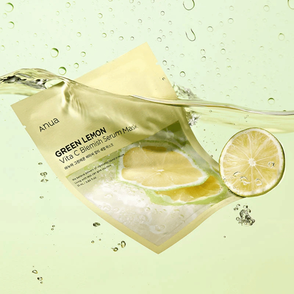 Une image vive de l'emballage de Anua Green Lemon Vita C Blemish Serum Mask avec des gouttes d'eau transparentes et des tranches de citron vert autour. L'emballage est partiellement recouvert par un flux d'eau sur un fond vert clair.