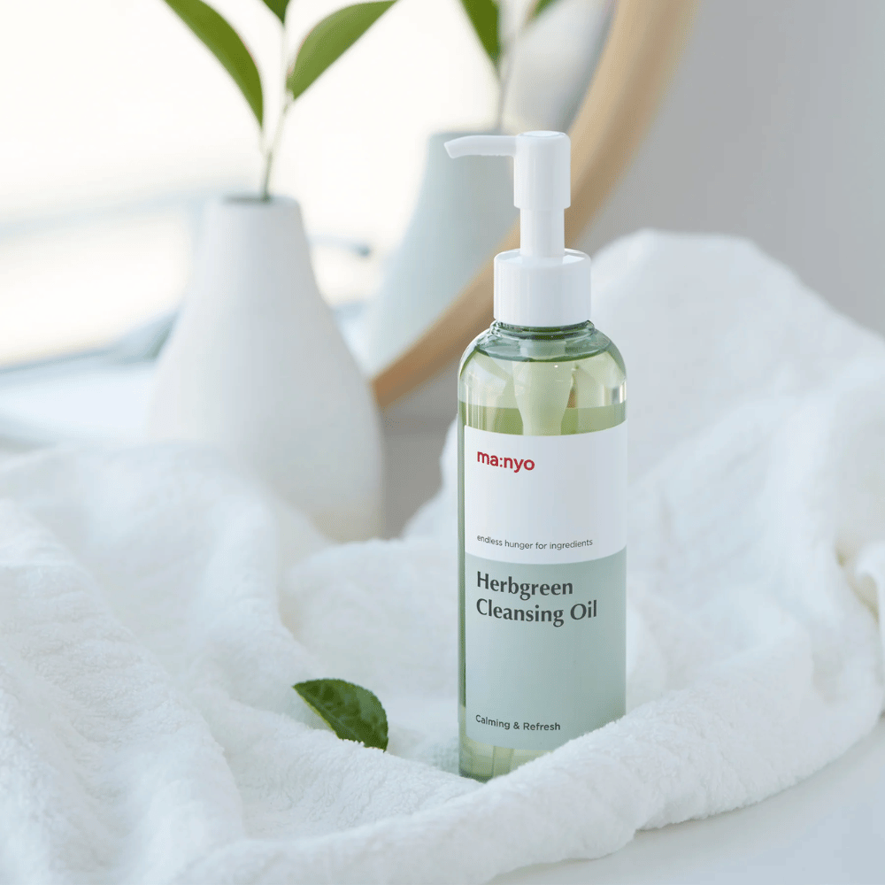 ma:nyo Herbgreen Cleansing Oil dans un flacon pompe placé sur une serviette blanche, huile nettoyante apaisante avec des ingrédients à base de plantes pour un nettoyage doux du visage