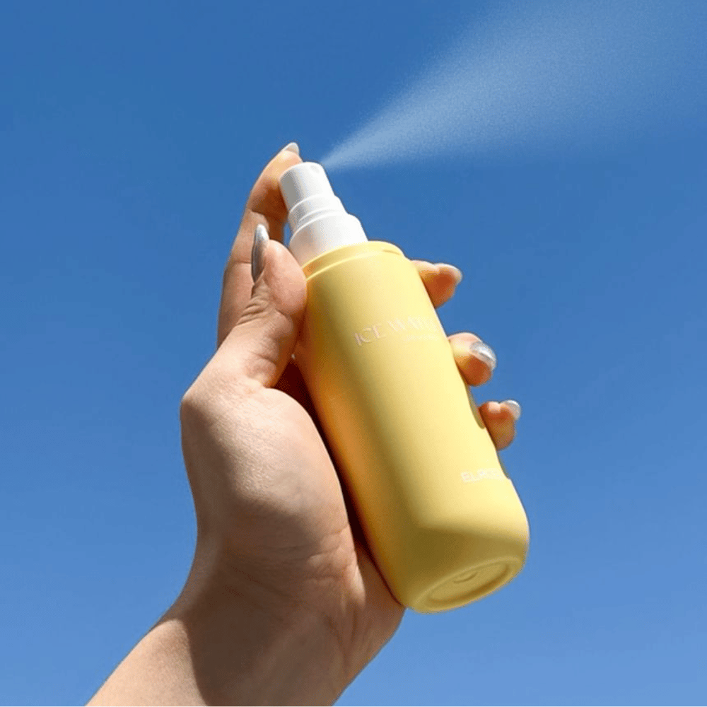 ELROEL Ice Water Sun Mist SPF 40 PA+++ brume solaire pulvérisée depuis un flacon vers un ciel bleu, protection solaire légère qui hydrate et rafraîchit la peau