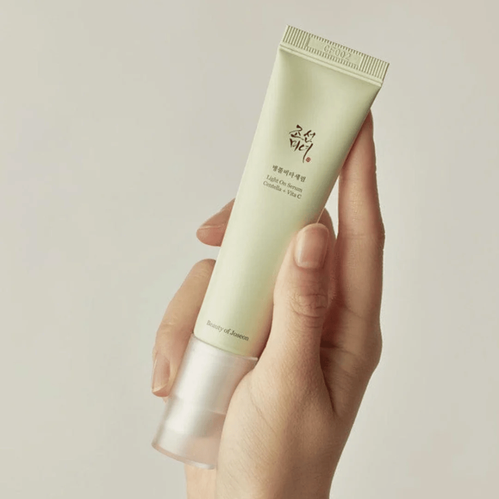 Une main tient le Beauty of Joseon Light On Serum avec Centella et vitamine C, dans un tube vert clair au design minimaliste sur un fond neutre.