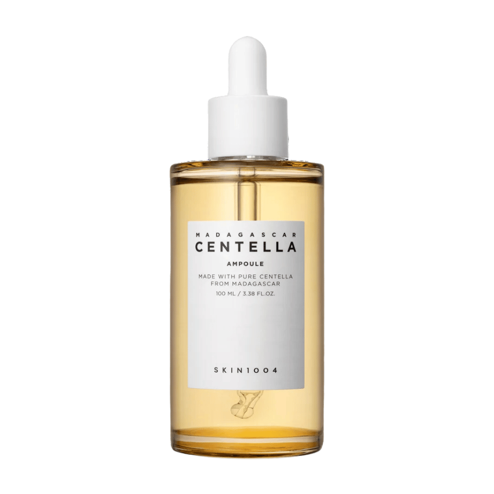L'image montre une bouteille de "Madagascar Centella Asiatica 100 Ampoule" de SKIN1004. La bouteille contient 100 ml et prétend être fabriquée avec de la centella pure de Madagascar. Le produit semble être un sérum de soin de la peau et l'étiquette simple donne une impression de pureté et de naturalité. La bouteille avec un bouchon compte-gouttes suggère qu'il s'agit d'un produit de soin de la peau soigneusement dosé.