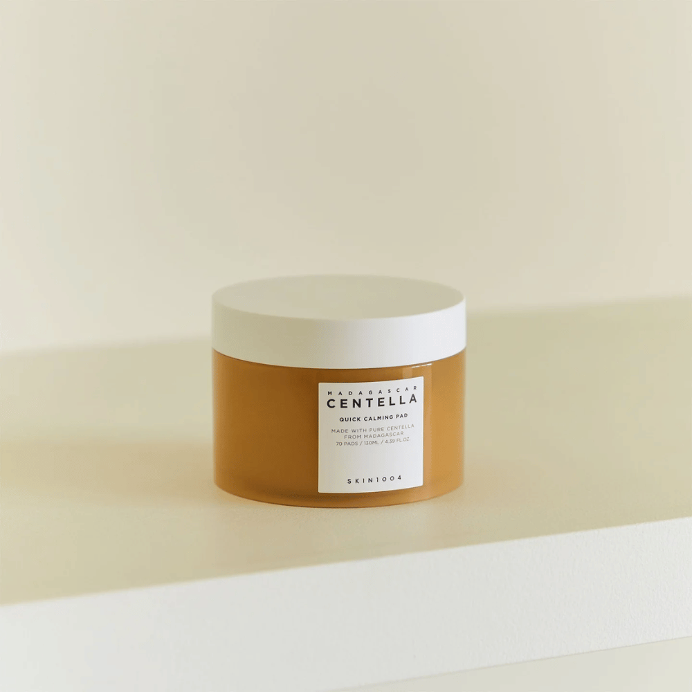 SKIN1004 Madagascar Centella Quick Calming Pad placé sur une étagère blanche – pot ambré avec couvercle blanc et étiquette claire à l'avant.