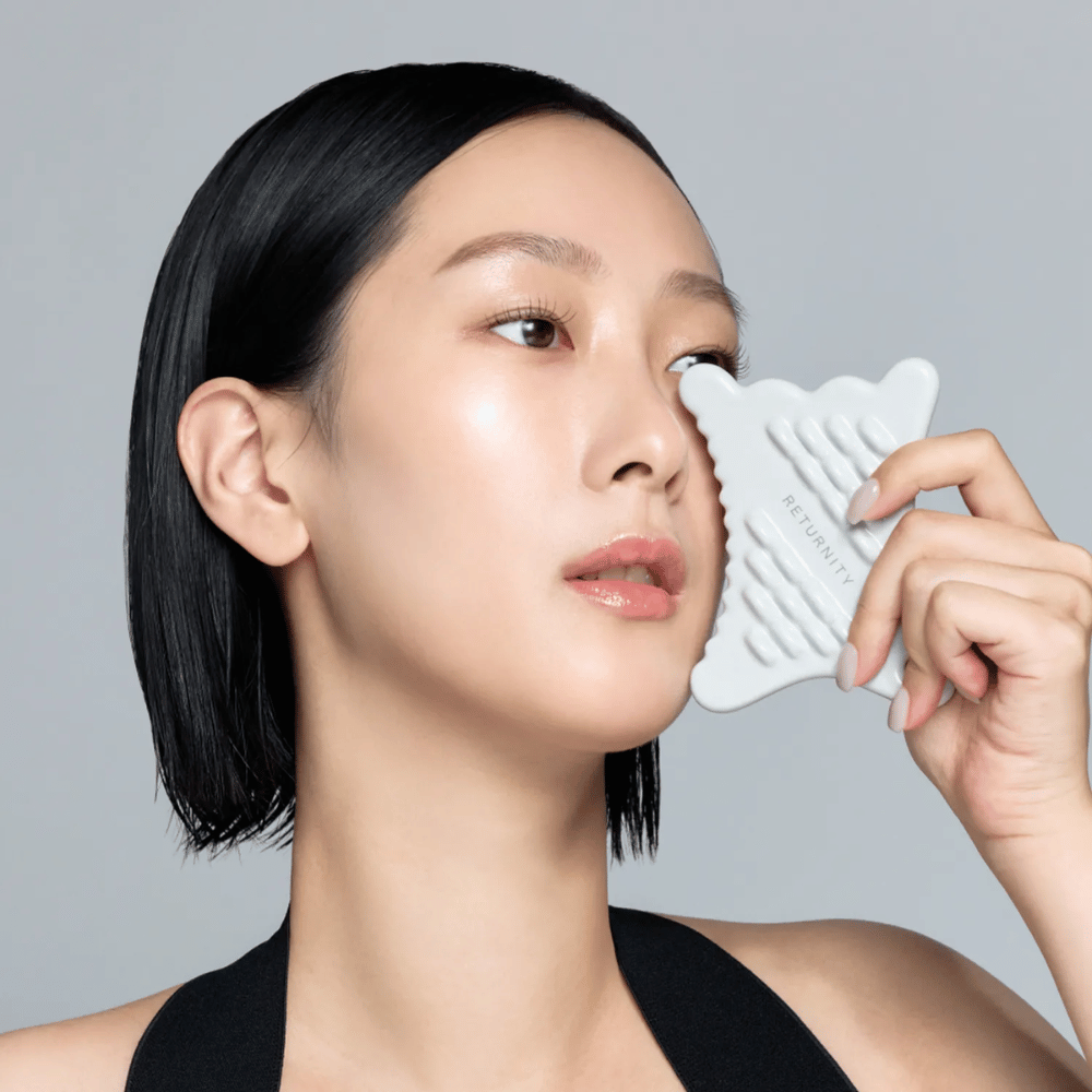 Gros plan sur un modèle utilisant RETURNITY Mini Guasha autour des yeux et des joues pour le massage et des soins relaxants de la peau.