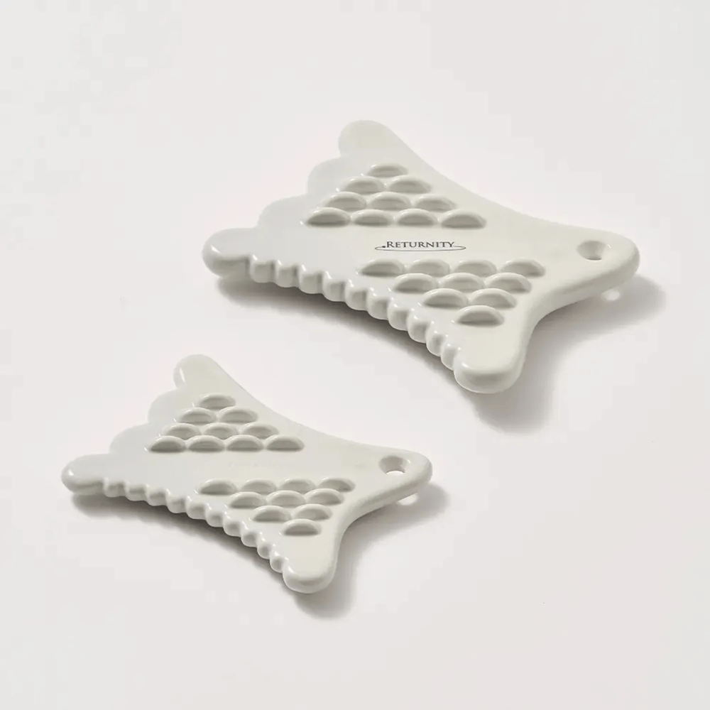 Deux outils RETURNITY Mini Guasha blancs à surface texturée et au design ergonomique sur fond clair.