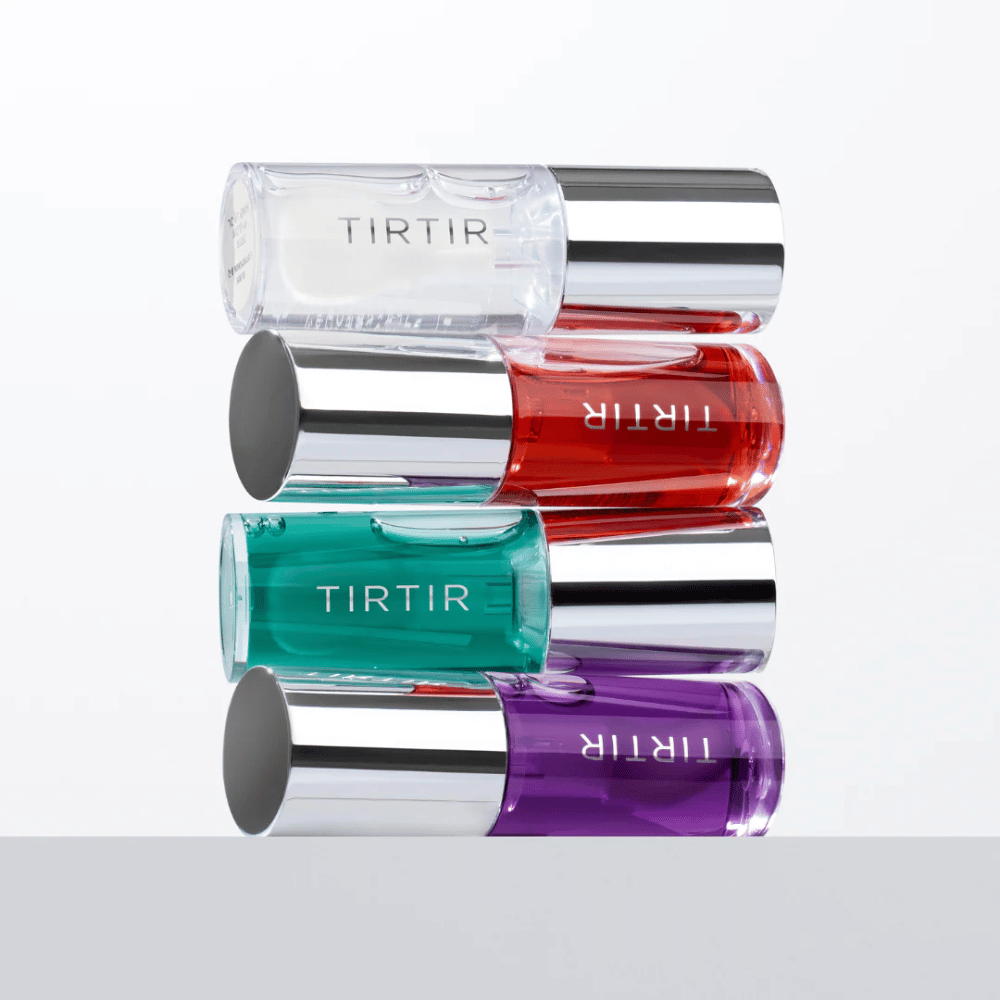 Quatre TIRTIR My Glow Lip Oil de différentes couleurs - transparent, rouge, vert et violet - empilés les uns sur les autres avec des couvercles argentés sur fond blanc.