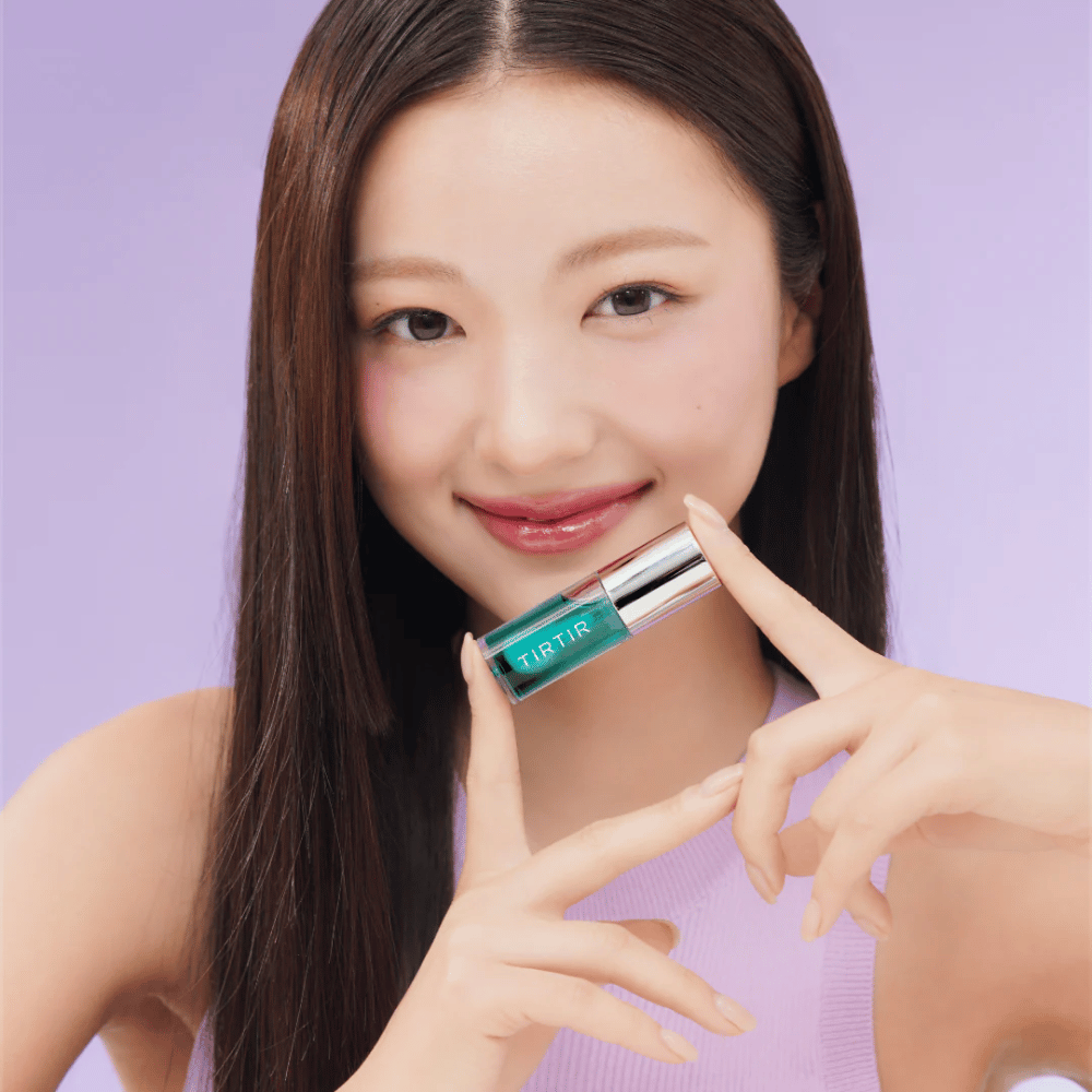 Femme aux cheveux longs et raides tenant un TIRTIR My Glow Lip Oil et montrant ses lèvres roses brillantes sur un fond violet.