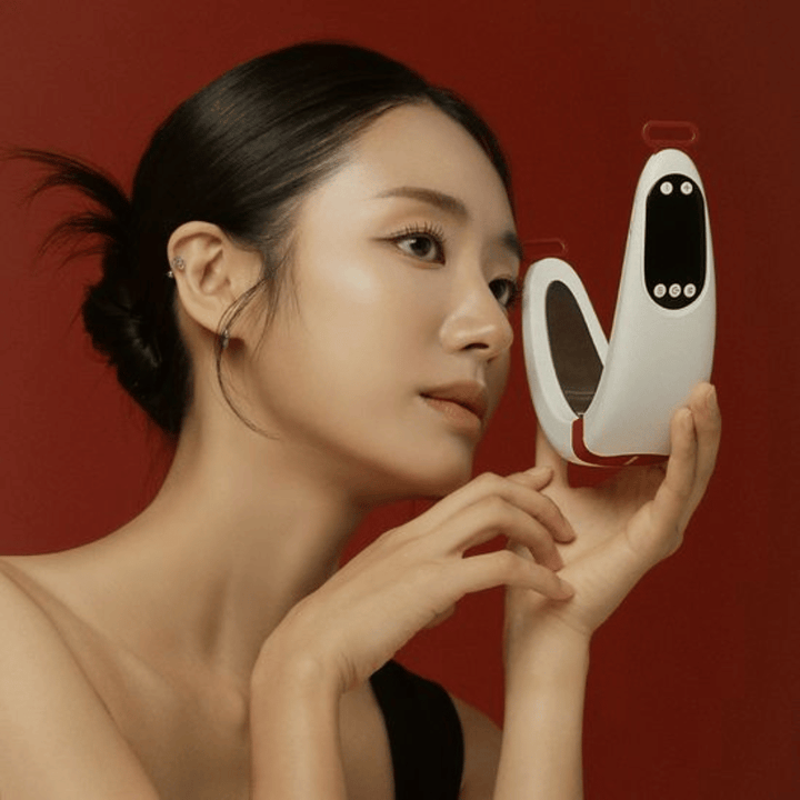 Un modèle tient Beaund Nmode Pro devant le visage sur un fond rouge. L’image met en valeur le design élégant de l’appareil, l’écran numérique et le format compact.