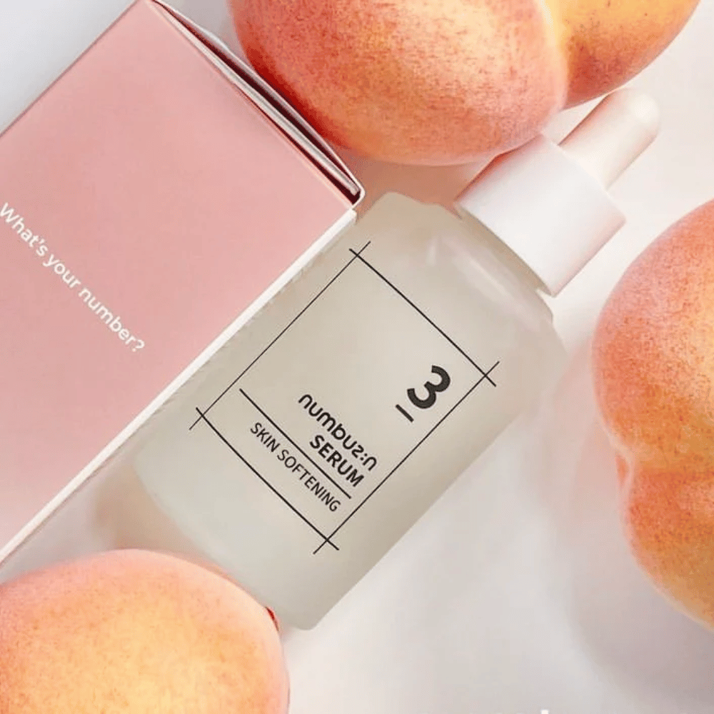 Flacon avec numbus:in No.3 Skin Softening Serum entouré de pêches et une boîte rose avec le texte "Quel est votre numéro ?".