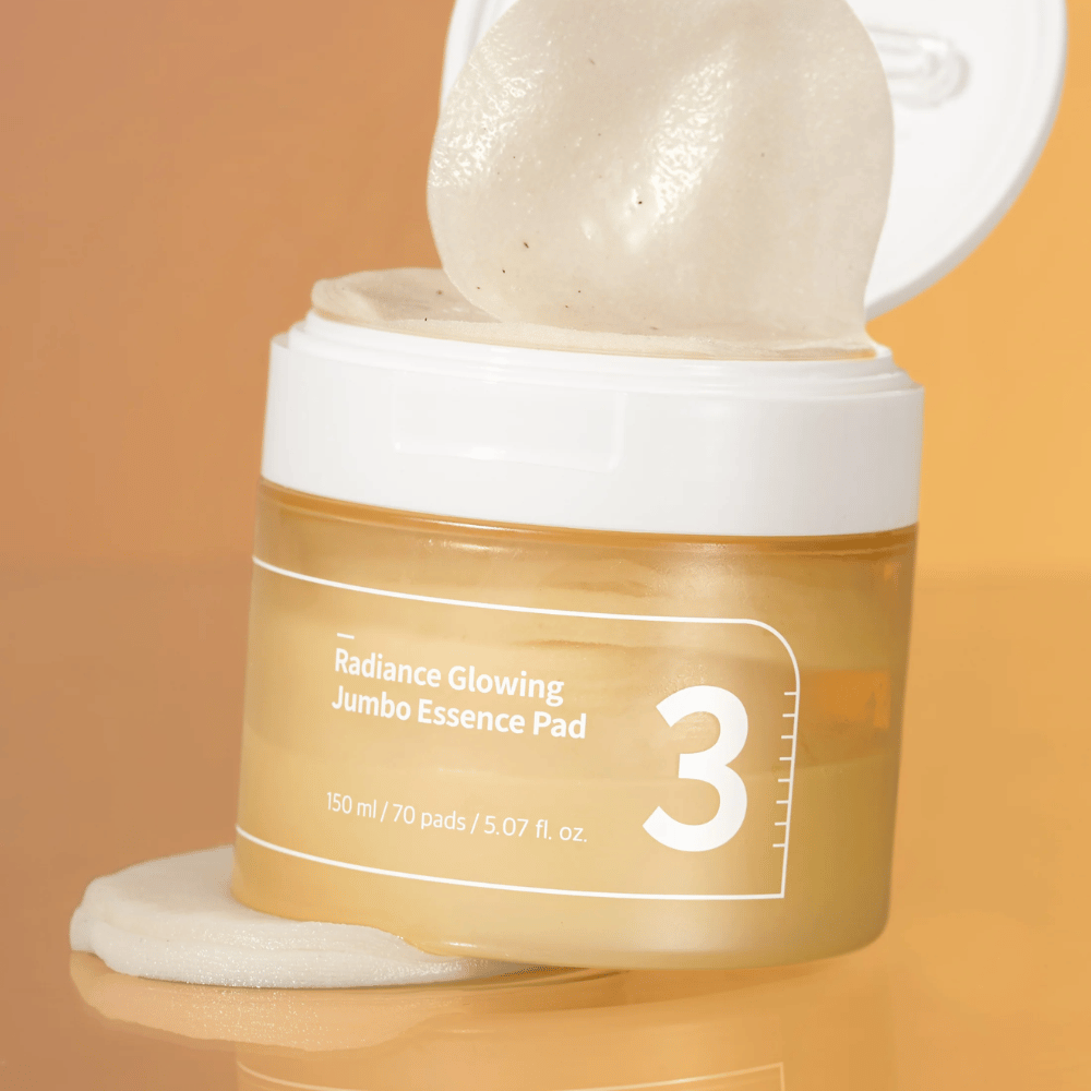 Öppen burk med numbuzin No. 3 Radiance Glowing Jumbo Essence Pad, en pad syns lutad mot kanten, bakgrund i orange ton.