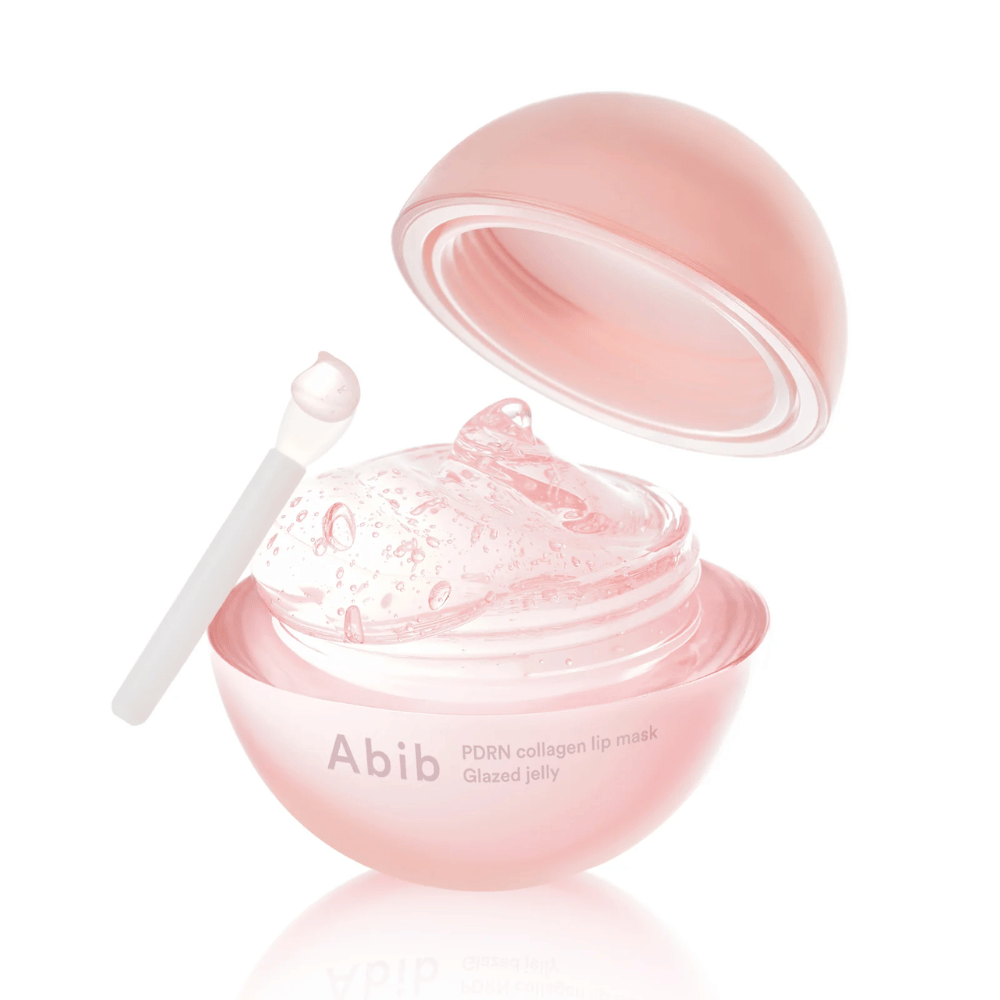 Boîte ronde rose avec Abib PDRN Collagen Lip Mask Glazed Jelly, ouverte avec le couvercle incliné vers l'arrière. Gel transparent avec des bulles d'air visible dans la boîte avec une petite spatule.