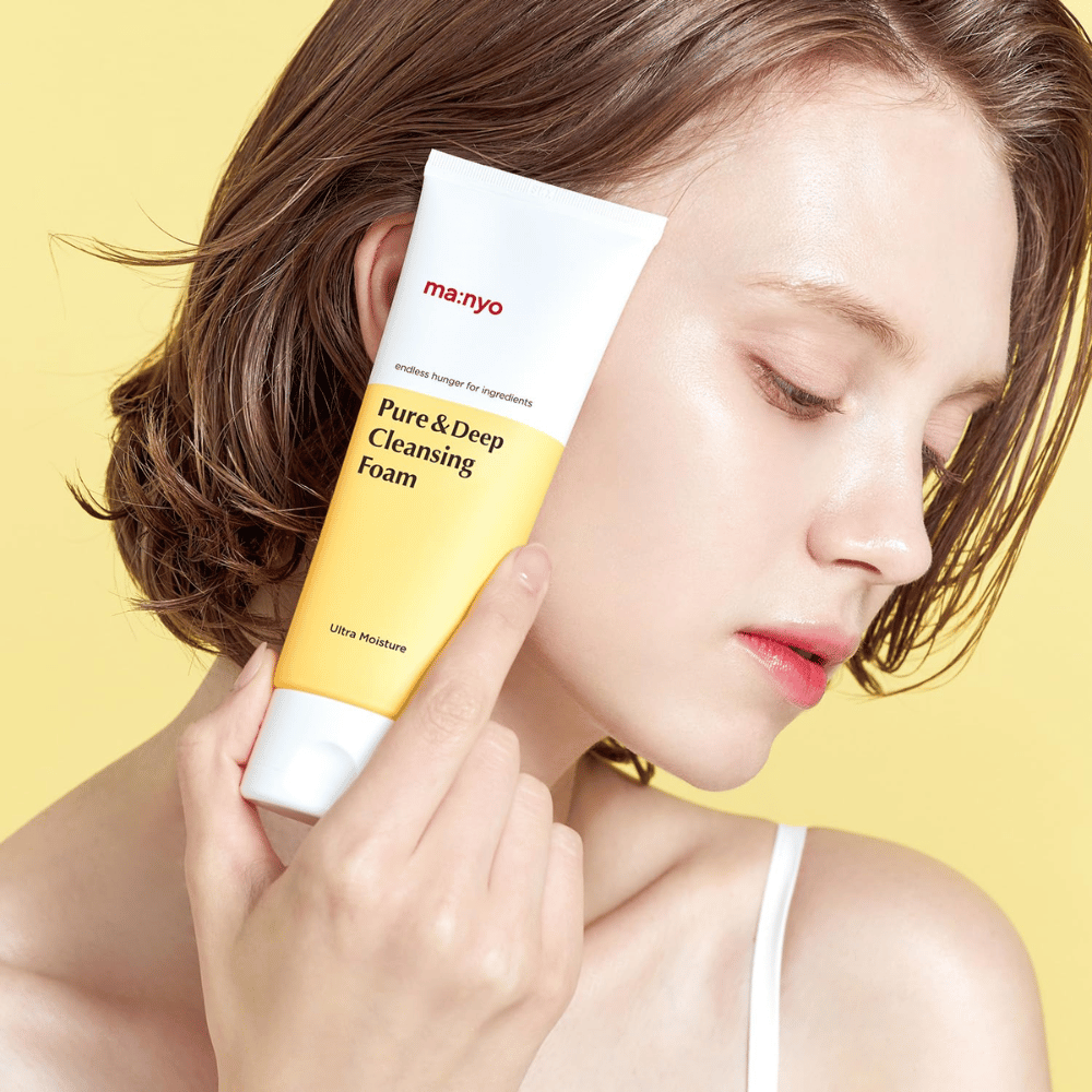 Femme avec une peau fraîche et hydratée tenant Ma:nyo Pure & Deep Cleansing Foam – nettoyant doux pour le visage qui apporte éclat et équilibre avec des ingrédients naturels.