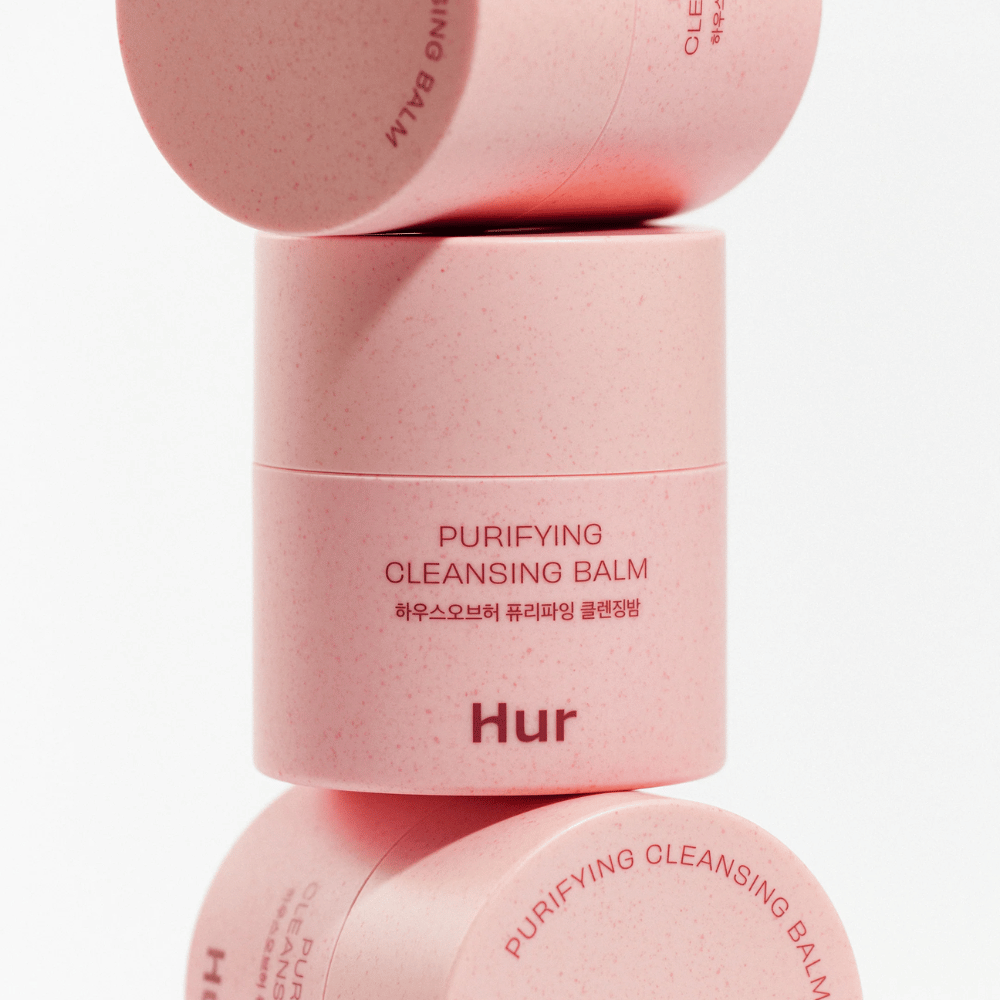 Comment Purifying Cleansing Balm dans un emballage rose empilé en studio. Baume nettoyant qui dissout efficacement le maquillage, le sébum et les impuretés sans dessécher la peau.