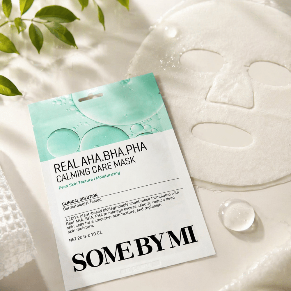 SOME BY MI Real AHA.BHA.PHA Calming Care Mask est présentée avec le masque en tissu déplié. Autour du produit, on voit des gouttes d’hydratation et des feuilles vertes qui renforcent la sensation d’hydratation, de soin apaisant et d’exfoliation douce. L’image met en avant l’accent du masque sur une texture de peau plus uniforme et un meilleur équilibre hydrique.