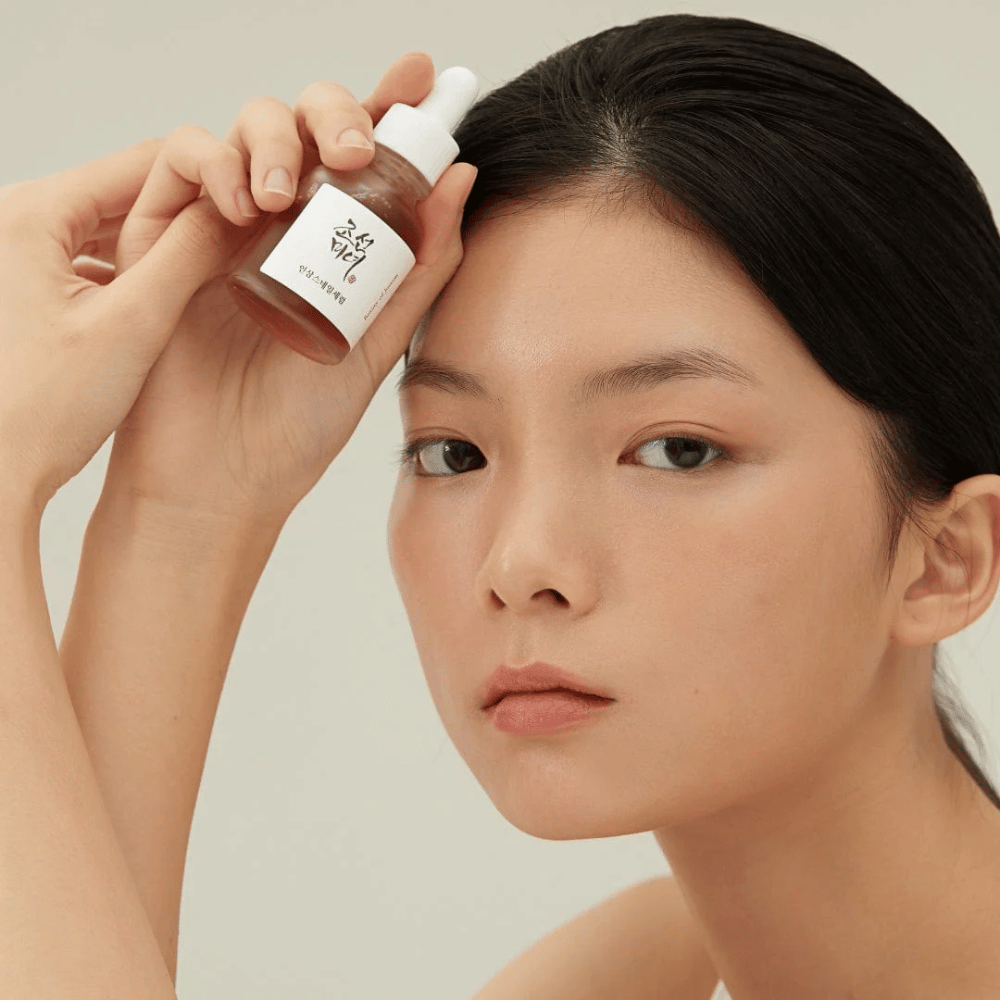 Le modèle tient Beauty of Joseon Revive Serum près de la joue – sérum nourrissant avec ginseng et mucine d'escargot.
