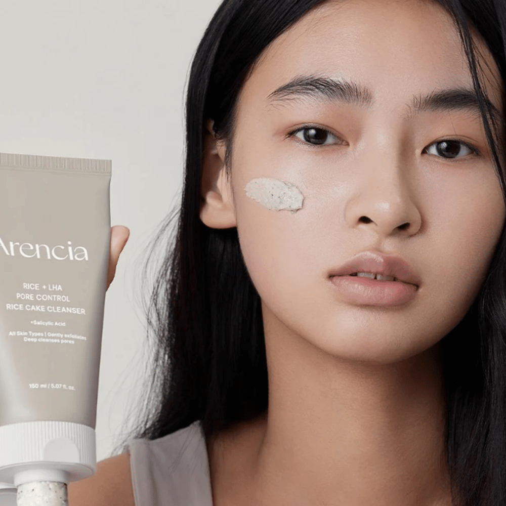 Modèle tenant Arencia Rice + LHA Pore Control Rice Cake Cleanser avec le produit appliqué sur la joue, illustrant un nettoyage des pores doux mais efficace pour une utilisation quotidienne.