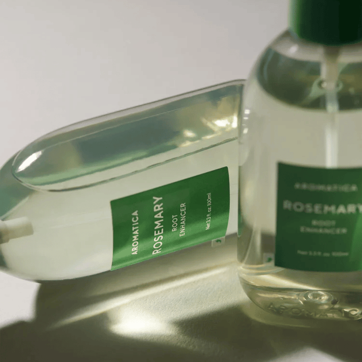 Deux bouteilles de AROMATICA Rosemary Root Enhancer avec capuchon de protection transparent et étiquette verte. Gros plan mettant en avant le design premium du produit et son concept de soin capillaire naturel.