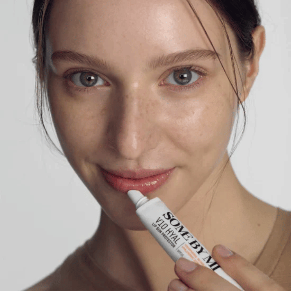 Une femme tient un tube V10 Hyal Lip Sun Protector SPF15 7ml de baume à lèvres pour la protection solaire et l'hydratation, de SOME BY MI.