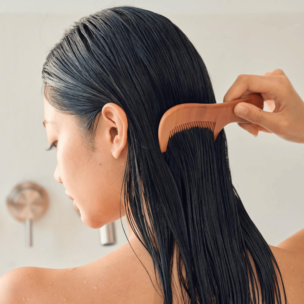 Une personne peigne de longs cheveux mouillés avec un peigne à dents larges après l’application de Heveblue Salmon Pullkeratin Centella Hair Treatment. Illustre l’effet démêlant et adoucissant pour un résultat plus lisse.
