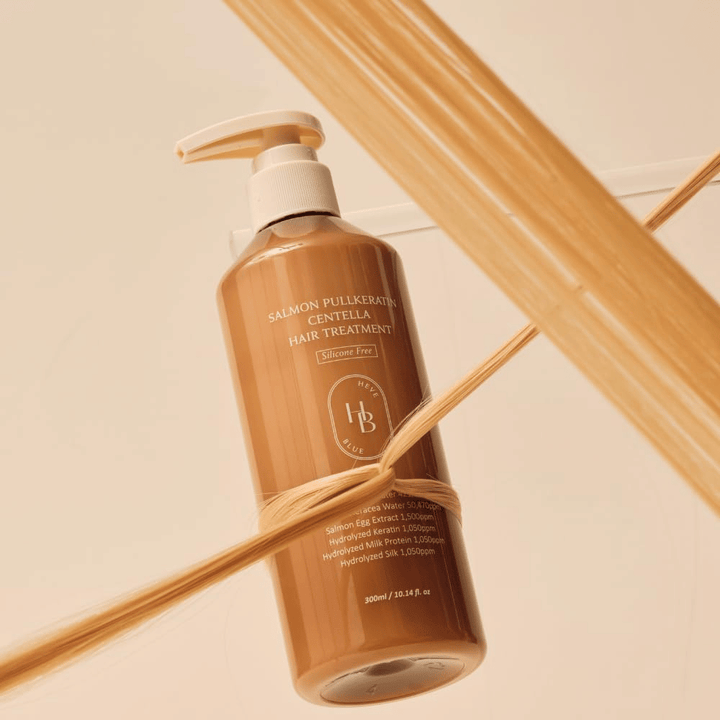 Heveblue Salmon Pullkeratin Centella Hair Treatment dans un flacon brun entouré de mèches de cheveux. L’image met en avant les propriétés nourrissantes du soin capillaire en mettant l’accent sur la brillance, la force et des cheveux soyeux.
