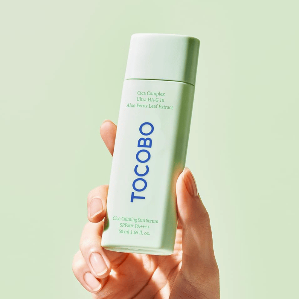 Main tenant TOCOBO Cica Calming Sun Serum avec emballage vert menthe et texte bleu sur fond vert clair.