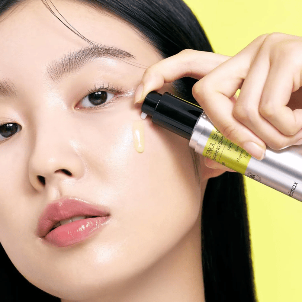 Un modèle applique The Vita-A Retinol Shot Tightening Serum de Tiam près de la zone des yeux, en mettant l'accent sur l'éclat de la peau et la consistance jaune du sérum.