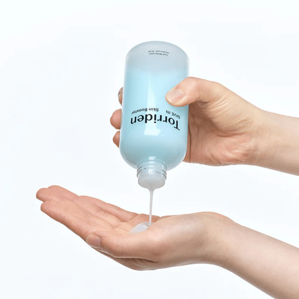 Des mains tenant une bouteille de produit de soin de la peau et distribuant un liquide clair dans la paume. La bouteille est étiquetée "Torriden - DIVE-IN Low Molecule Hyaluronic Acid Skin Booster".