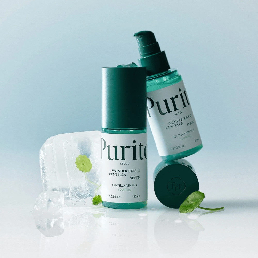 Deux bouteilles de Purito Wonder Releaf Centella Serum, une debout et une couchée, entourées de glaçons avec des feuilles de centella à l'intérieur ainsi qu'une feuille détachée sur une surface bleu clair.
