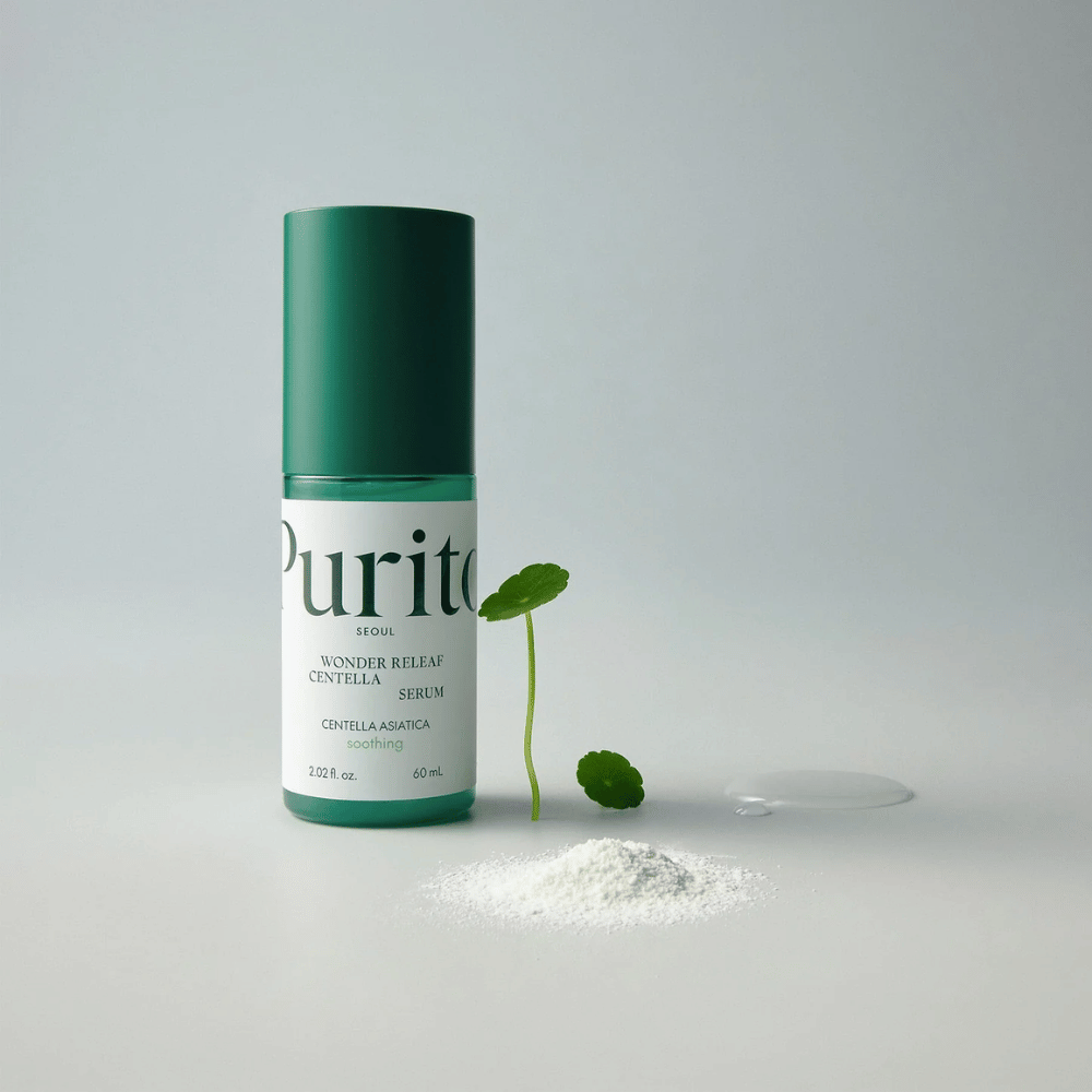 Bouteille verte de Purito Wonder Releaf Centella Serum 60 ml posée sur une surface blanche, entourée de feuilles de centella, d'une goutte de sérum transparent et d'une petite poudre blanche.
