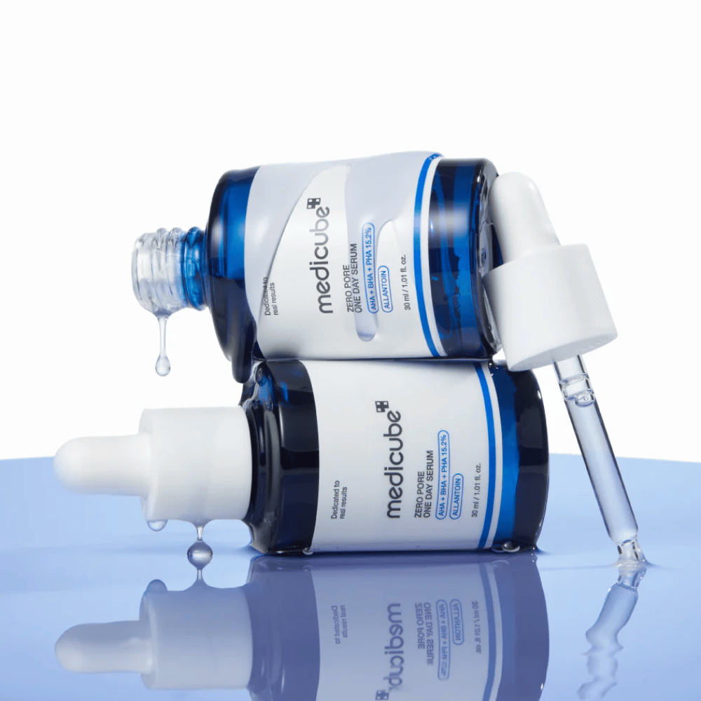 Deux bouteilles bleues de Medicube Zero Pore One Day Serum posées l'une contre l'autre, avec pipettes et gouttes de sérum sur une surface bleue réfléchissante.